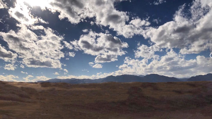 Blue mountain range with brown field, white clouds and yellow sun